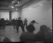 DESCRIPTION TE2/1977/64nTai-chi demonstration and talk. Begins with a quick cut, a view of a large white room with chairs. Cuts to an out-of-focus zoom and darkened shot an unknown object. Cuts to an elongated, white-washed brick wall gallery space. A seated audience looks on a demonstration from three sides of the room. The 2 men at the focus of this demonstration (Cameron, left, and Cuthbert, right) face the audience, their backs to a blank wall. The handheld camera is shooting off-right the r